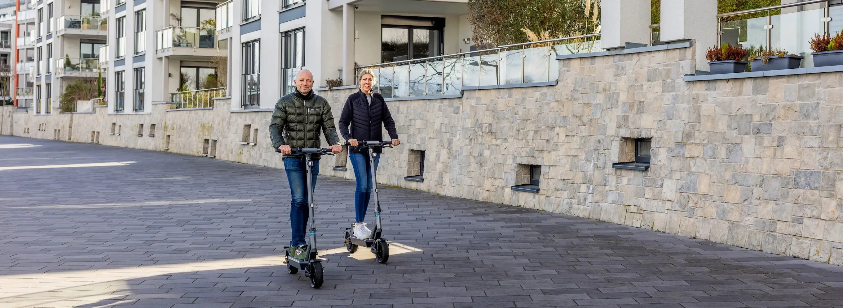 e-Scooter Fuehrerschein Versicherung Helm Zwei Erwachsene fahren rechtlich zugelassene Elektroroller im städtischen Straßenverkehr ohne Führerscheinpflicht und mit vorgeschriebener Haftpflichtversicherung als Beispiel gesetzeskonformer Elektromobilität.