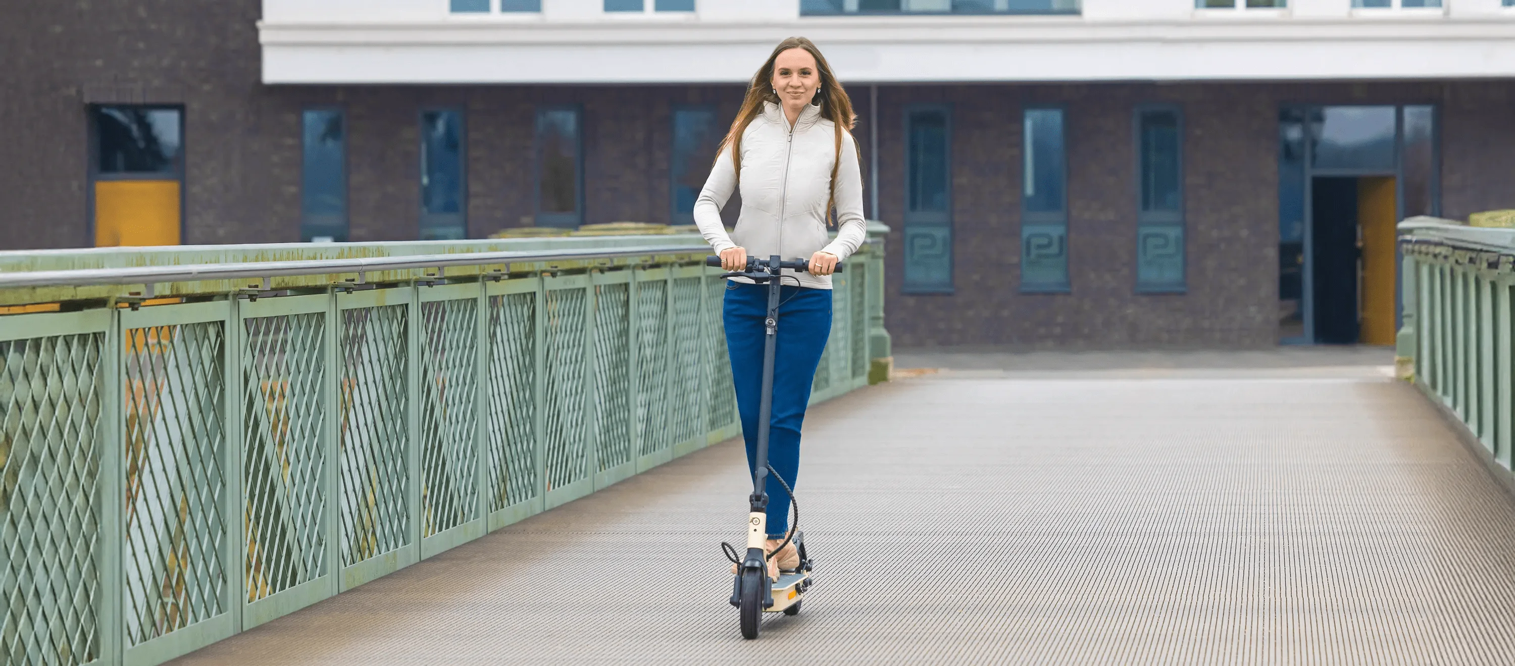 Fahrerin auf ePF-1 Elektroroller fährt über eine Brücke – leichter und kompakter E-Scooter für nachhaltige Mobilität und urbane Fortbewegung