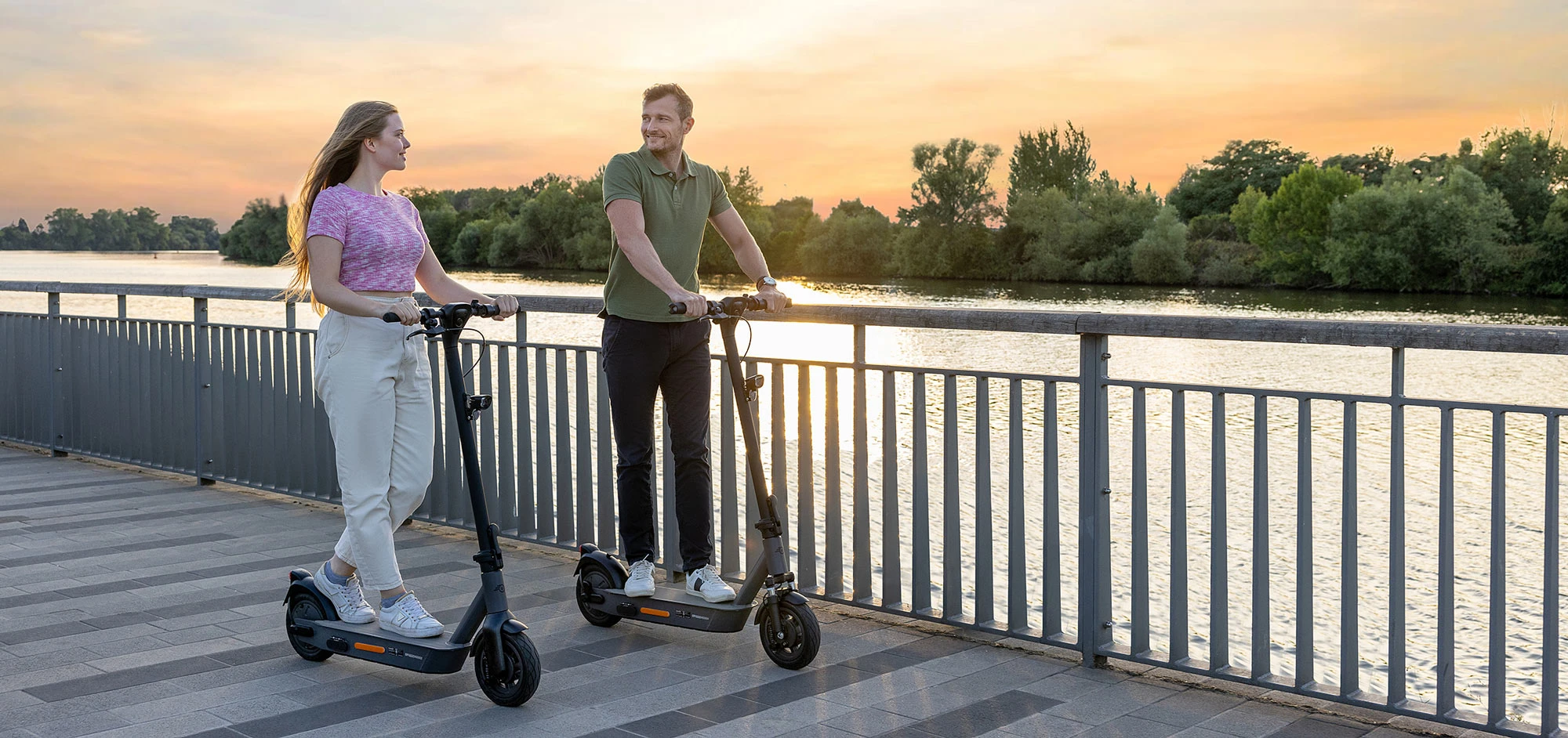 Zwei Fahrer auf ePF-2 Elektrorollern am Rhein bei Sonnenuntergang – stilvolle E-Scooter mit Straßenzulassung, ideal für nachhaltige Mobilität und entspannte Fahrten in der Abendsonne