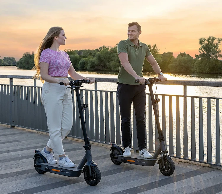 Zwei Fahrer auf ePF-2 Elektrorollern am Rhein bei Sonnenuntergang – stilvolle E-Scooter mit Straßenzulassung, ideal für nachhaltige Mobilität und entspannte Fahrten in der Abendsonne