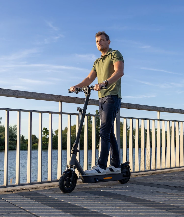 Mann fährt mit dem ePF-2 Elektroroller bei Sonnenschein über eine Brücke – leichter E-Scooter mit Straßenzulassung für komfortable, nachhaltige Mobilität im Alltag