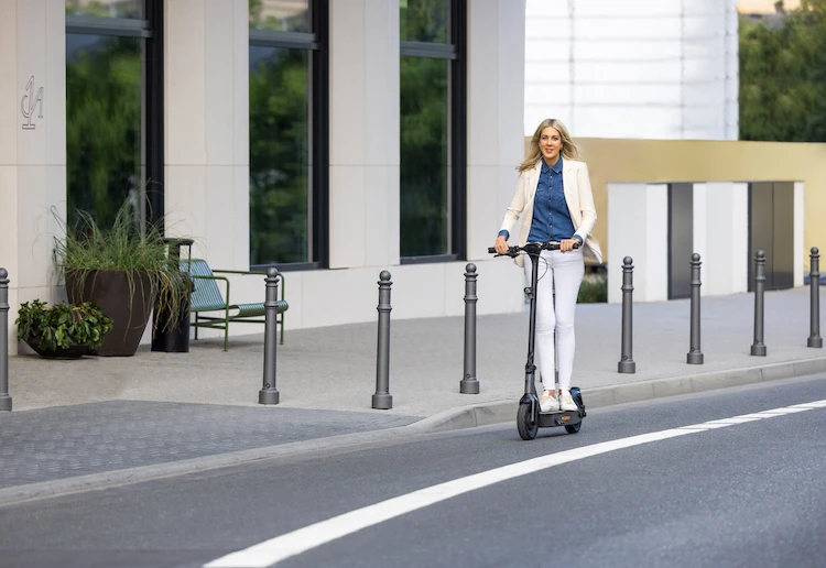Fahrerin auf dem ePF-2 Elektroroller vor modernem Gebäudekomplex – eleganter E-Scooter mit Straßenzulassung für stilvolle und nachhaltige Mobilität in der Stadt