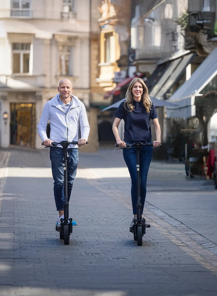 Zwei Erwachsene fahren mit ePF-2 PRO E-Scootern durch die Altstadt – Elektroroller mit Straßenzulassung für nachhaltige Mikromobilität, ideal für Pendler und urbane Mobilität.