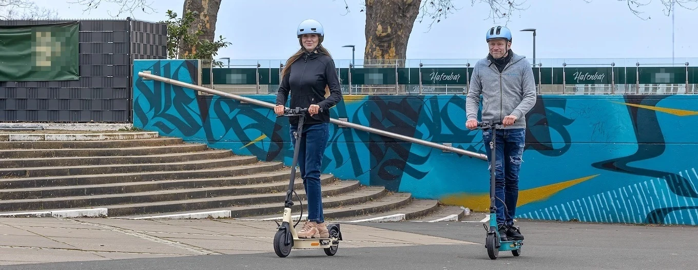 e-scooter Versicherung Helm Zwei Erwachsene fahren auf kompakten e-Scootern mit Schutzhelm – Sicherheitstipp: immer einen Helm tragen.