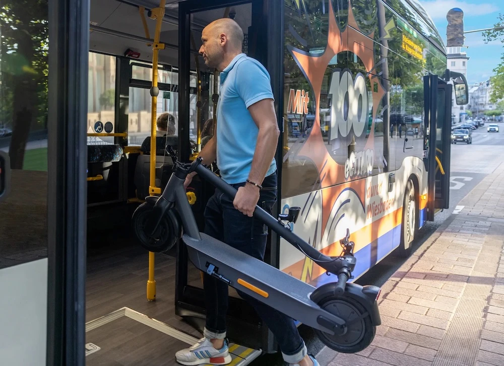 e-scooter mobil stadt Pendler mit klappbarem e-Scooter steigt in einen Stadtbus ein und kombiniert nachhaltige Elektromobilität und Mikromobilität mit öffentlichen Verkehrsmitteln.