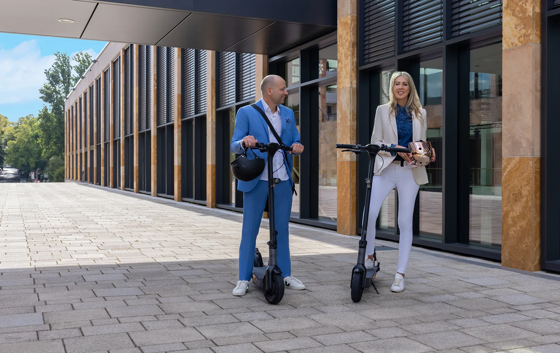 Zwei Personen stehen mit ihren ePF-2 Elektrorollern vor moderner Gebäudefassade – klappbare E-Scooter für urbane Mobilität, nachhaltige Fortbewegung und flexible Pendlerlösungen